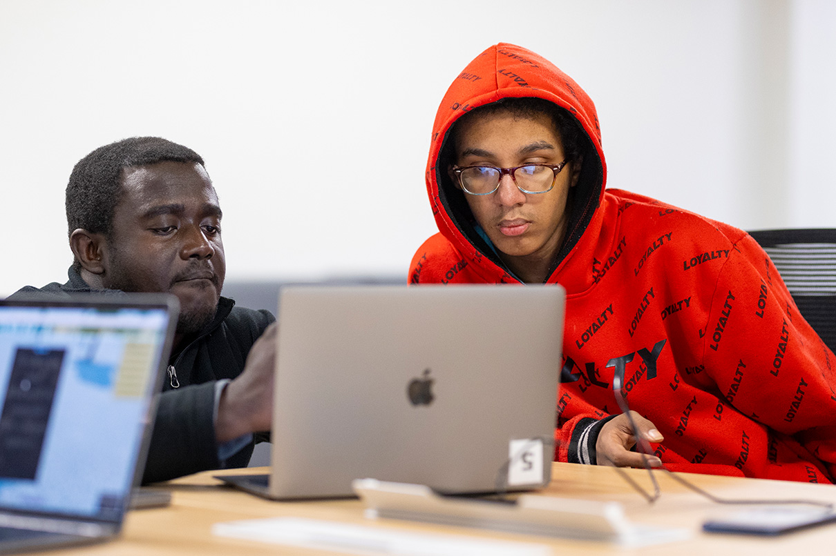 Two dae students in classroom working on laptops with focus