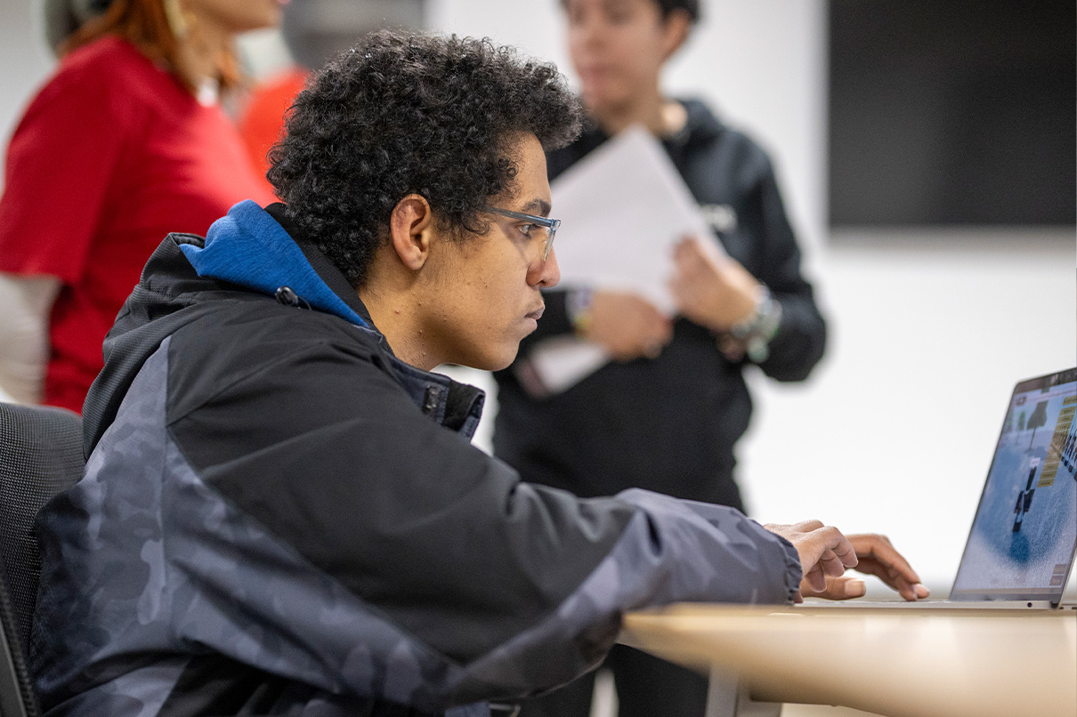 dae student working on laptop in classroom, with focus
